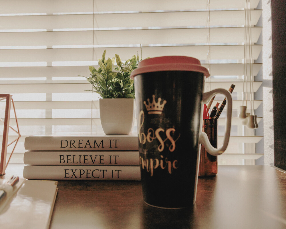 dream it, believe it, expect it books stacked in a row on a desktop next to a mug with girl boss written on it. 